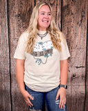 A girl modeling the Tough Luck Cowboy Graphic Tee in front of a wooden back drop.