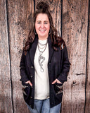 A woman wearing the Stand by Me Knit Sweater with both hands in her pockets while standing in front of a wood back drop.