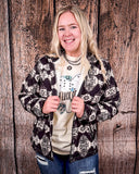 A girl wearing the Aztec City Soft Shell Jacket. The jacket is open and she is gripping the sides of the jacket where the zipper is. She is standing in front of a wood back drop.