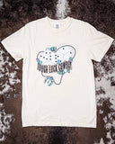 The Tough Luck Cowboy Graphic Tee displayed on cowhide.