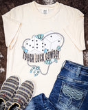 The Tough Luck Cowboy Graphic Tee displayed on cowhide along with jeans and shoes.
