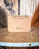 The back of the  Outlander Edge Credit Card Holder in Beige displayed on a wooden table with wheat behind it, sitting in front of a wood backdrop.
