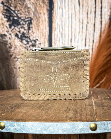 The Outlander Edge Credit Card Holder in Brown displayed on a wooden table with wheat behind it, sitting in front of a wood backdrop.