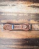The Lone Star Hand Tooled Leather Watch Band in Light Saddle Tan sitting on a ruler to show size. It is being displayed on a wooden table.