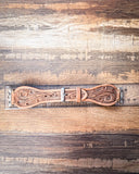 The Lone Star Hand Tooled Leather Watch Band in Light Saddle Tan sitting on a ruler to show size. It is displayed on a wooden table.