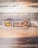 The Lone Star Hand Tooled Leather Watch Band in Antique Tan sitting on a ruler to show size, displayed on a wooden table.