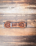 The Lone Star Hand Tooled Leather Watch Band in Antique Saddle Brown sitting on a ruler to show size, displayed on a wooden table.