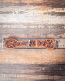 The Lone Star Hand Tooled Leather Watch Band in Antique Saddle Brown sitting on a ruler to show size, displayed on a wooden table.