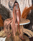 Side view of the Loralei Hair on Hide Fringe Crossbody Bag, displayed on a wooden table with wheat behind it. It is sitting in front of a wood back drop.