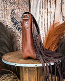 Side view of the Straybird Hair on Hide Fringe Crossbody Bag displayed on a wooden table with wheat behind it. It is sitting in front of a wood back drop.