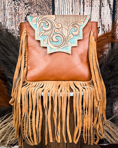 The Sunny Jo Fringe Crossbody Bag displayed on a wooden table with wheat behind it, sitting in front of a wood back drop.