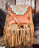 The Sunny Jo Fringe Crossbody Bag displayed on a wooden table with wheat behind it, sitting in front of a wood back drop.