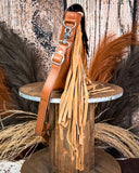 Side view of the Sunny Jo Fringe Crossbody Bag, being displayed on a wooden table. There is wheat and a wood back drop behind it.
