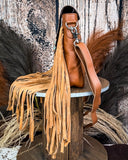 Side view of the Sunny Jo Fringe Crossbody Bag, displayed on a wooden table. There is wheat and a wood back drop behind it.