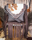 The Mae Hair on Hide Fringe Crossbody Bag displayed on a wooden table with wheat behind it, sitting in front of a wood back drop.