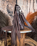 Side view of the Mae Hair on Hide Fringe Crossbody Bag, displayed on a wooden table with wheat behind it. It is sitting in front of a wood back drop.