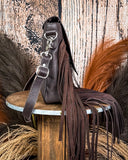 Side view of the Mae Hair on Hide Fringe Crossbody Bag, displayed on a wooden table with wheat behind it. It is sitting in front of a wood back drop.
