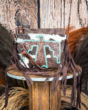 The Quill Hair on Hide Fringe Crossbody Bag displayed on a wooden table with wheat behind it, sitting in front of a wood back drop.
