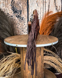 Side view of the Quill Hair on Hide Fringe Crossbody Bag, being displayed on a wooden table. There is wheat and a wood back drop behind it.