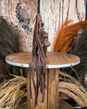 Side view of the Quill Hair on Hide Fringe Crossbody Bag, being displayed on a wooden table. There is wheat and a wood back drop behind it.