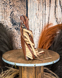 Side view of the Lariat Hair on Hide Fringe Crossbody Bag, being displayed on a wooden table with wheat grass and a wood back drop behind it.