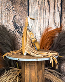 Side view of the Talon Hair on Hide Fringe Crossbody Bag, being displayed on a wooden table with wheat grass and a wood backdrop behind it.