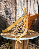 Side view of the Talon Hair on Hide Fringe Crossbody Bag, displayed on a wooden table with wheat grass and a wood backdrop behind it.