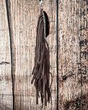 Side view of the Reveena Hair on Hide Fringe Phone Crossbody Bag, hanging from a hook. There is a wood backdrop behind it.