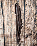 The Reveena Hair on Hide Fringe Phone Crossbody Bag, hanging from a hook. There is a wood backdrop behind it.