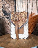 The Vesper Hair on Hide Phone Crossbody Bag, displayed on a wooden table with wheat grass and a wood backdrop behind it.