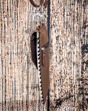 Side view of the Vesper Hair on Hide Phone Crossbody Bag, hanging from a hook. There is a wood backdrop behind it.