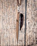 Side view of the Vesper Hair on Hide Phone Crossbody Bag, hanging from a hook. There is a wood backdrop behind it.