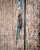 Side view of the Lark Hair on Hide Phone Crossbody Bag, hanging from a hook. There is a wood backdrop behind it.