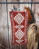 The Myna Mesa Towel, clipped to a hanger that is hanging from a metal rod with wheat behind it in a wood back ground.