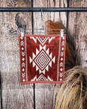The Myna Mesa hand towel clipped to a hanger that is hanging from a metal rod with wheat behind it in a wooden back ground.