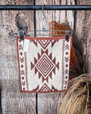 The back of the Myna Mesa hand towel, clipped to a hanger that is hanging from a metal rod with wheat behind it in a wooden back ground.