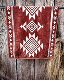 The Myna Mesa Towel hanging from a metal rod with wheat behind it in a wood background.