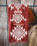 The Myna Mesa Towel set hanging from a rod with wheat behind it in a wood back ground.