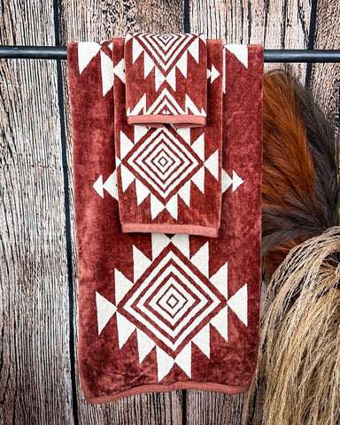The Myna Mesa Towel set hanging from a rod with wheat behind it in a wood back ground.