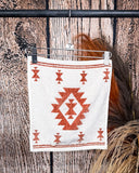 The Terra Sands face towel, clipped to a hanger that is hanging from a metal rod with wheat behind it in a wood back ground.