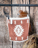 The back of the Terra Sands face towel, clipped to a hanger that is hanging from a metal rod with wheat behind it in a wood back ground.