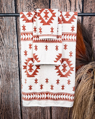 The Terra Sands Towel set hanging from a metal rod with wheat behind it in a wooden back ground.