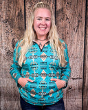 A model wearing the Laramie Kreek Fitted Pullover with both of her hands in the pockets in a wood back ground.