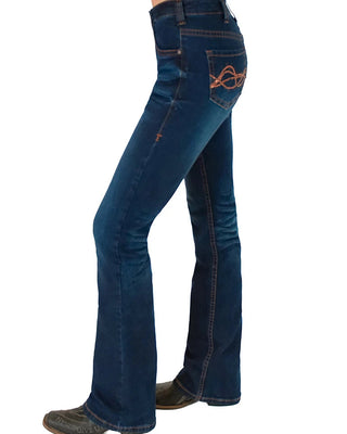 A side profile view of a person wearing dark blue flare jeans with orange contrast stitching and a matching orange embroidered logo on the back pocket, paired with dark boots against a white background.