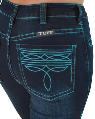 Close-up of the back pocket of dark blue denim jeans with turquoise contrast stitching and a decorative embroidered pattern. A small black brand patch reading TUFF is visible above the pocket.