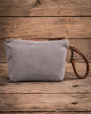 A gray fabric wristlet pouch with a brown leather wrist strap and zipper, displayed on a rustic wooden plank background.