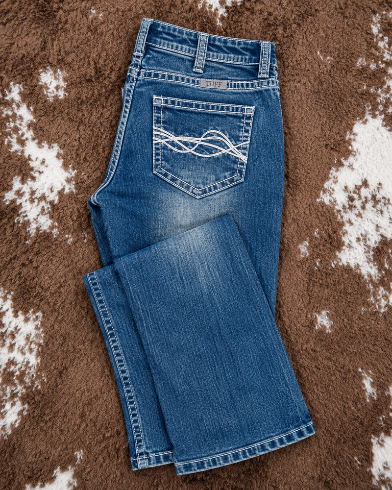 A pair of medium-wash blue jeans laid flat on a brown and white cowhide rug. The back pocket features a distinctive white embroidered wave pattern.