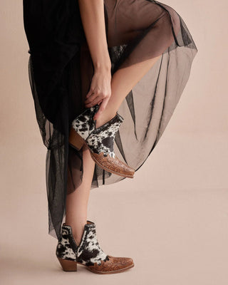 Person wearing a black dress with sheer overlay and cow print boots on a beige background