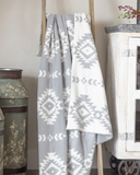 Gray and white patterned blanket draped over a wooden rack with decorative vases and a cabinet in the background.