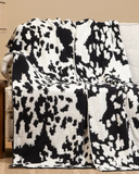Black and white cowhide patterned blanket draped over a couch in a living room setting.